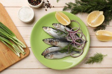 Photo of Fresh raw sprats, cut lemon, onion, dill and spices on light wooden table, flat lay