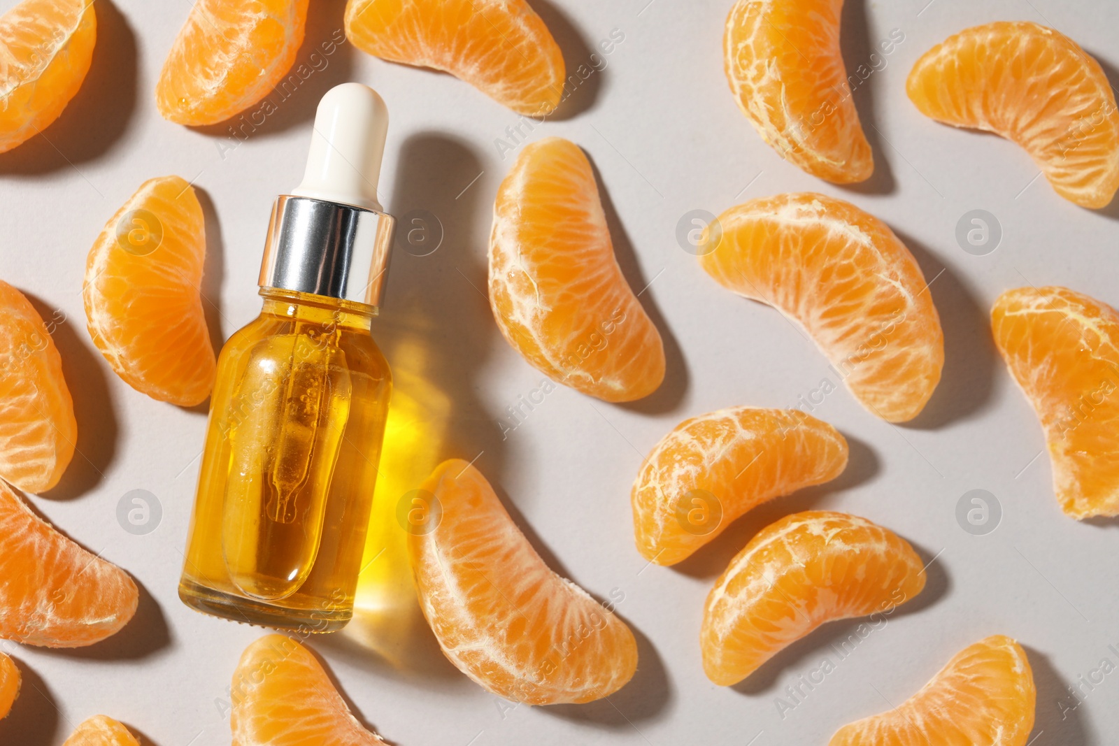 Photo of Aromatic tangerine essential oil in bottle and citrus fruit on grey table, flat lay