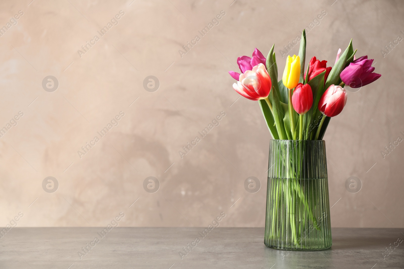 Photo of Beautiful spring tulips in vase on table against light background. Space for text