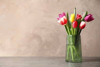 Photo of Beautiful spring tulips in vase on table against light background. Space for text