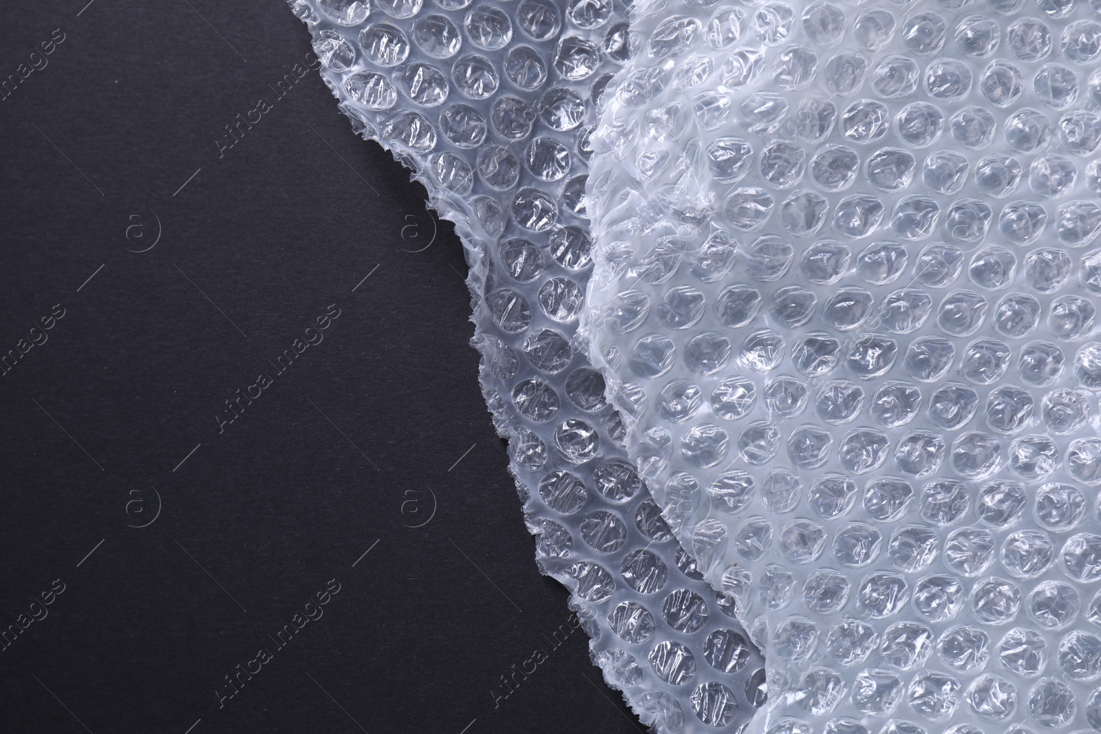 Photo of Transparent bubble wrap on black background, top view. Space for text