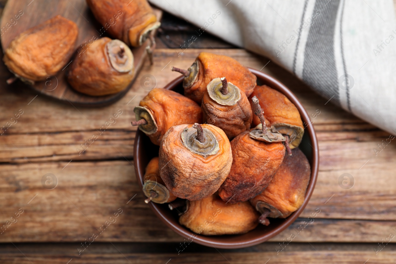 Photo of Bowl with tasty dried persimmon fruits on wooden table, flat lay