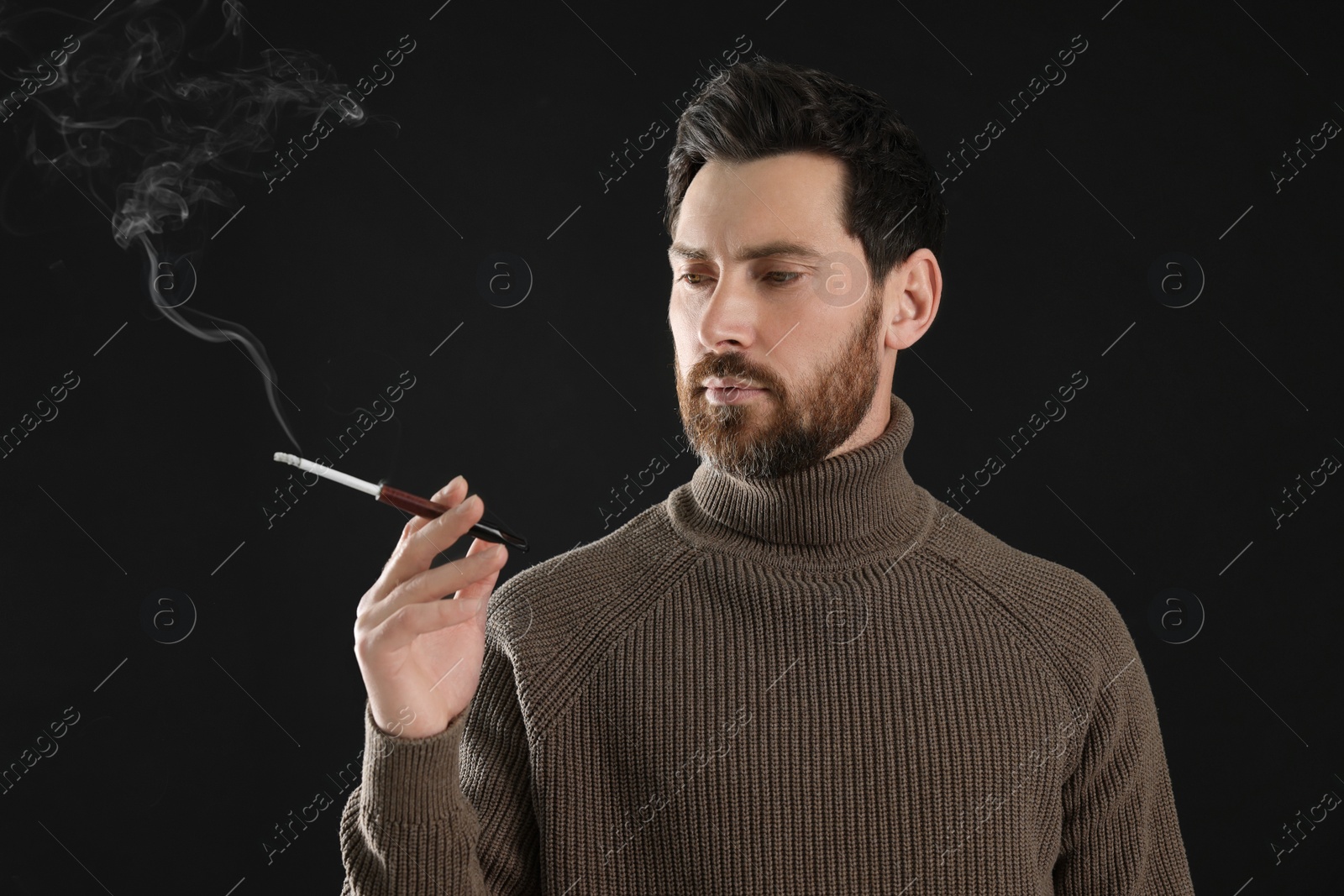 Photo of Man using cigarette holder for smoking on black background