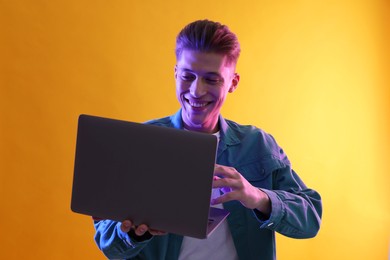 Photo of Young man with laptop talking via video chat on yellow background