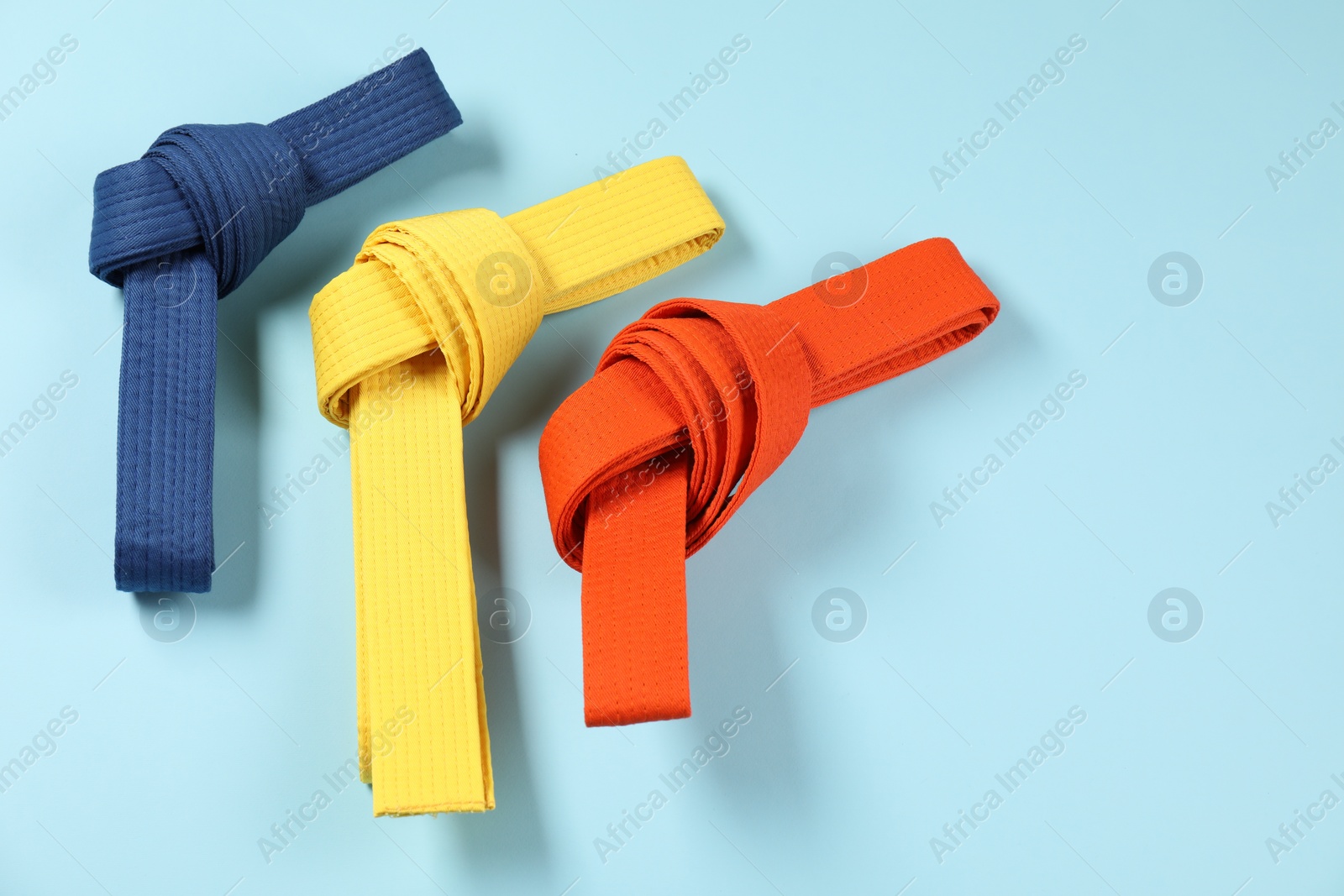 Photo of Colorful karate belts on light blue background, flat lay. Space for text