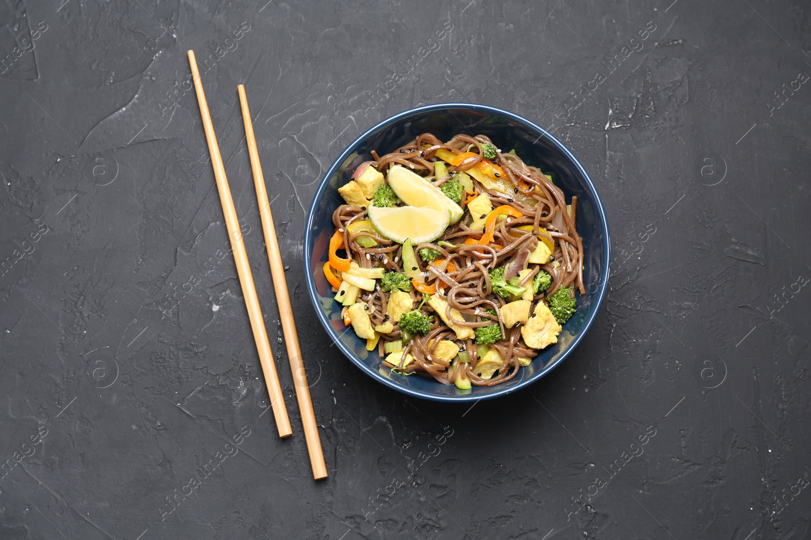 Photo of Stir-fry. Delicious cooked noodles with chicken and vegetables in bowl served on gray textured table, flat lay