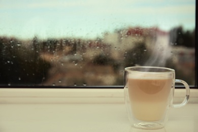 Cup of delicious hot drink on window sill. Space for text