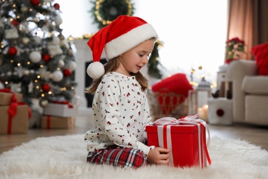 Cute little girl sitting with gift box in room decorated for Christmas