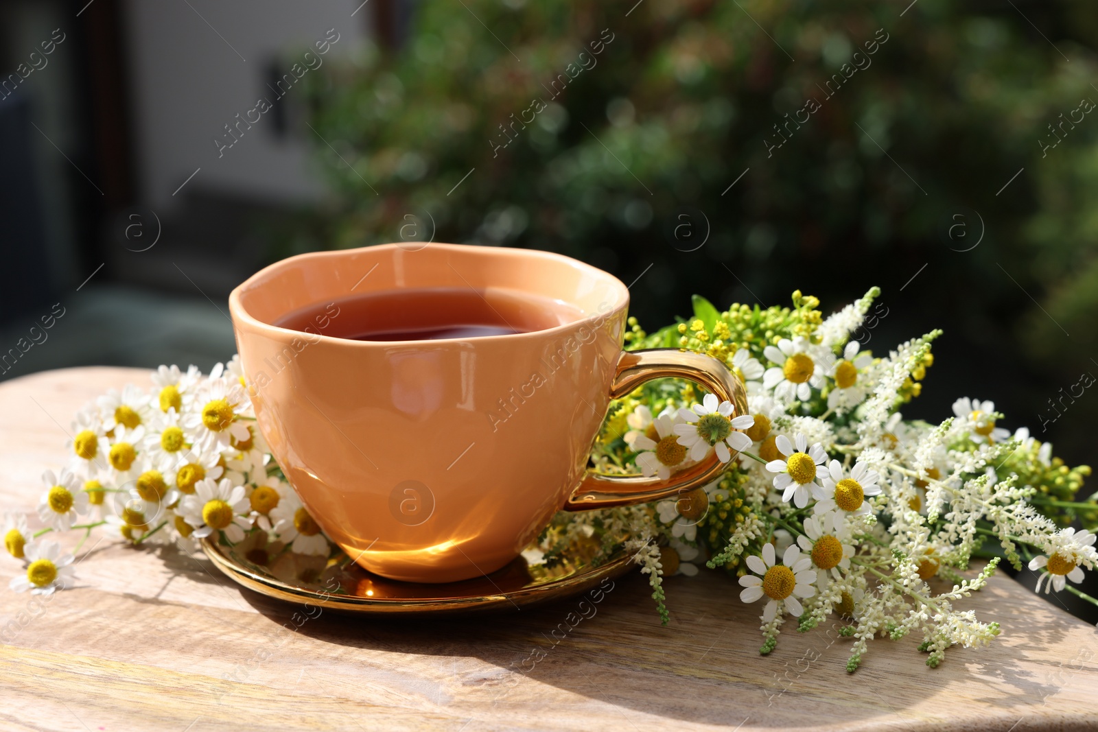 Photo of Cup of delicious chamomile tea and fresh flowers outdoors on sunny day