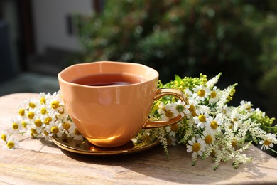 Cup of delicious chamomile tea and fresh flowers outdoors on sunny day