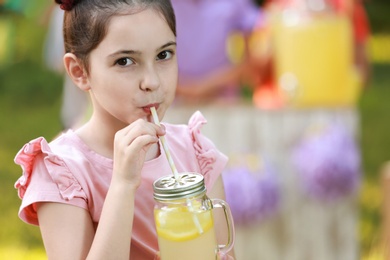 Photo of Cute little girl drinking natural lemonade in park, closeup with space for text. Summer refreshing beverage