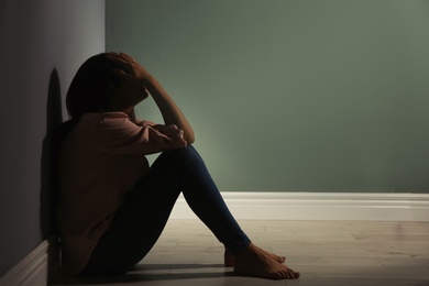 Photo of Depressed young woman sitting on floor in darkness