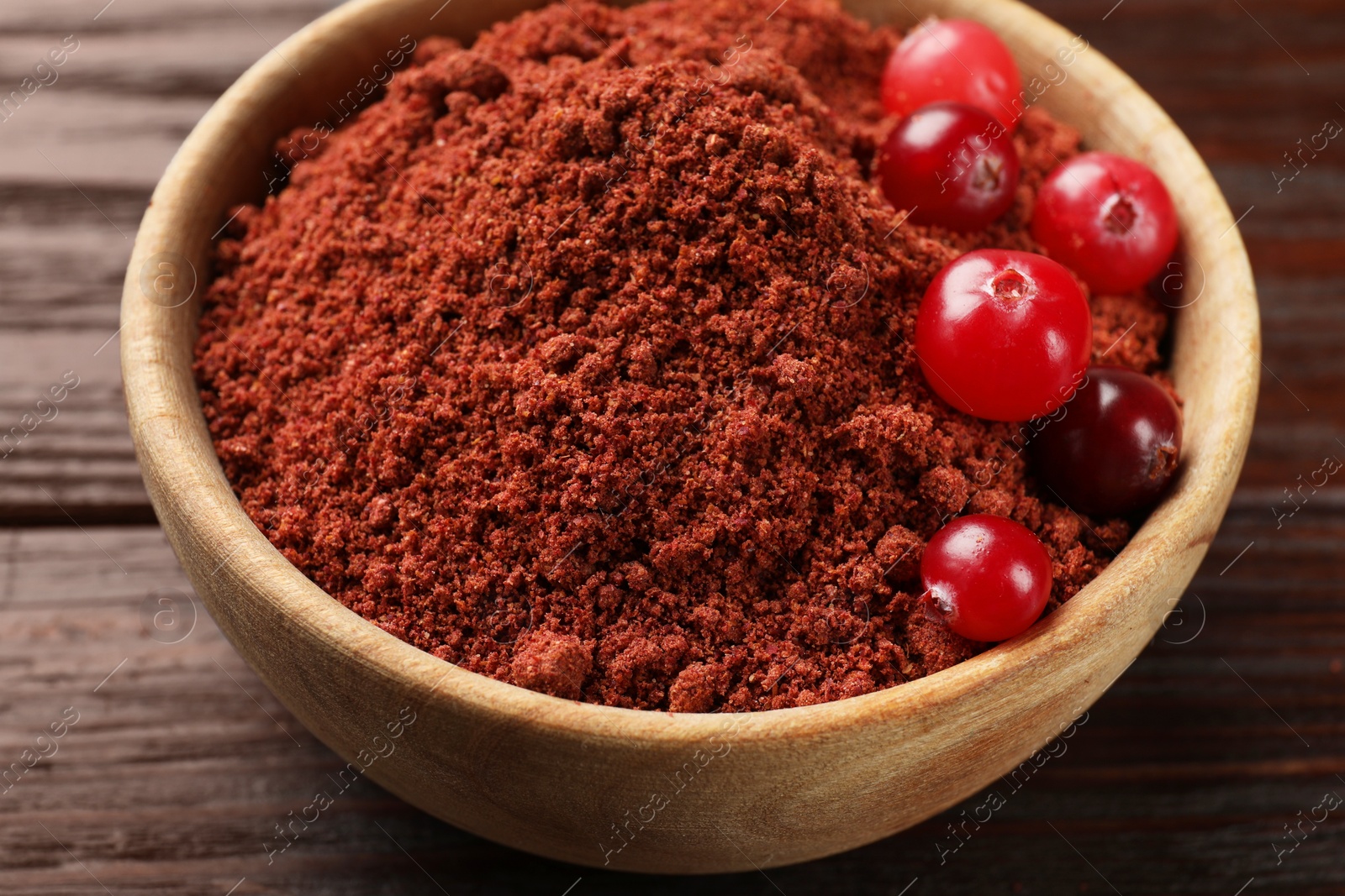 Photo of Dried cranberry powder and fresh berries in bowl on wooden table, closeup