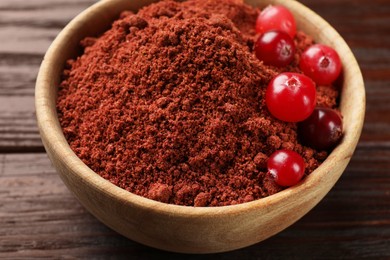 Dried cranberry powder and fresh berries in bowl on wooden table, closeup