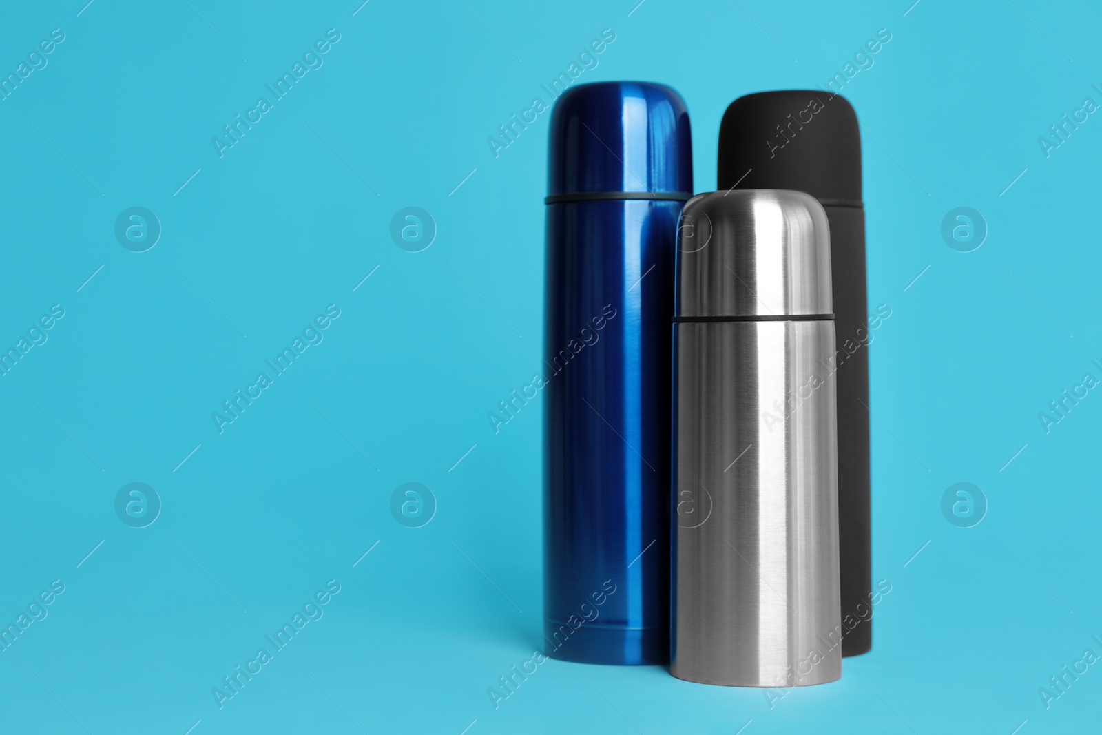 Photo of Stylish thermo bottles on light blue background, space for text