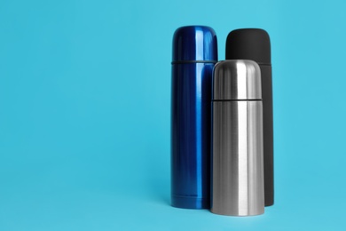 Photo of Stylish thermo bottles on light blue background, space for text