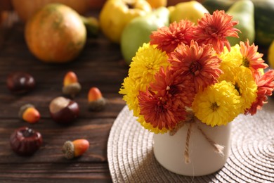 Photo of Beautiful colorful chrysanthemum flowers, chestnuts and acorns on wooden table, space for text. Autumn still life