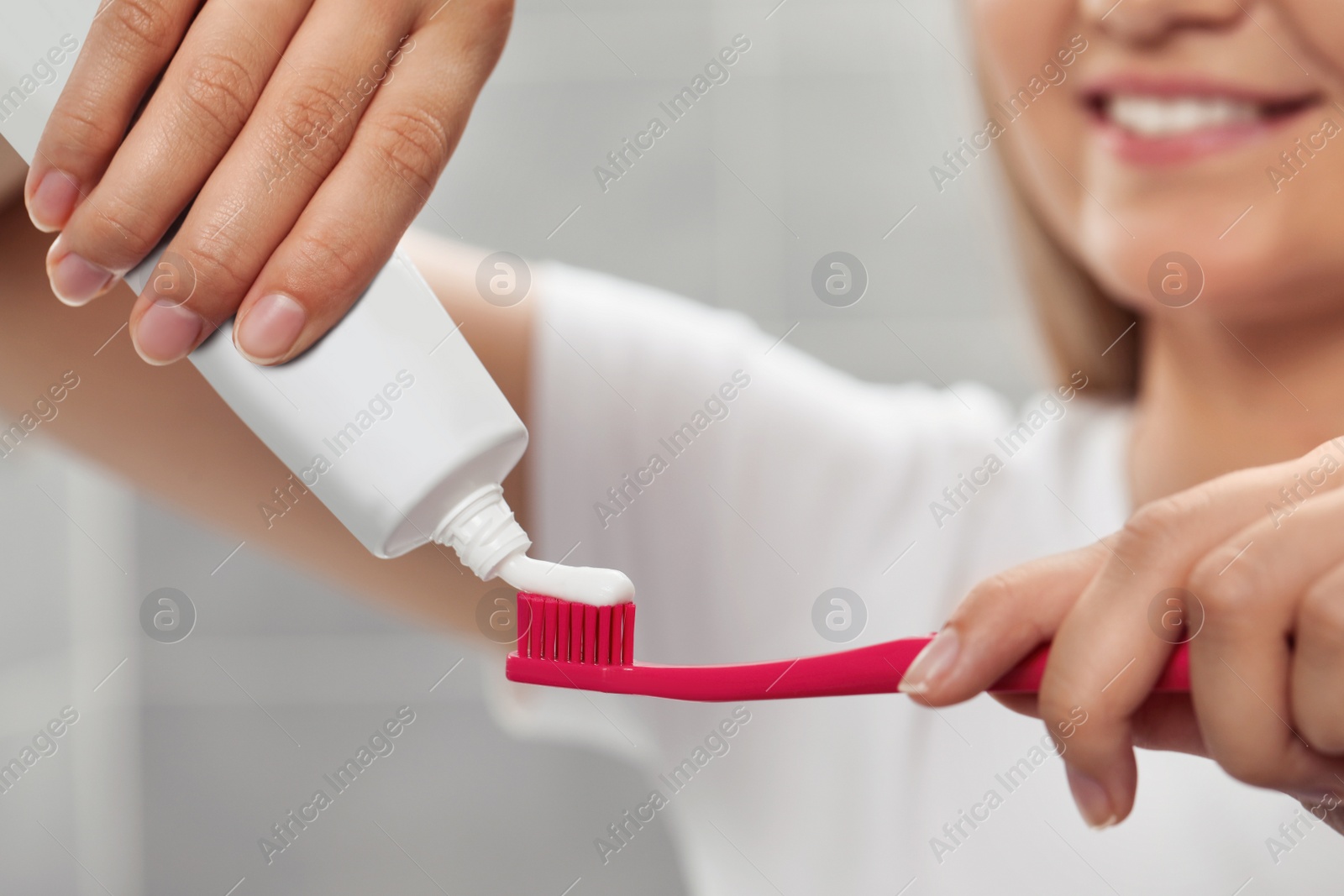 Photo of Woman applying toothpaste on brush in bathroom, closeup