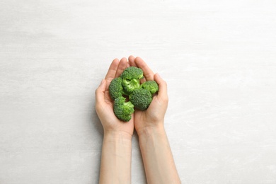 Photo of Young woman holding fresh broccoli over light grey table, top view