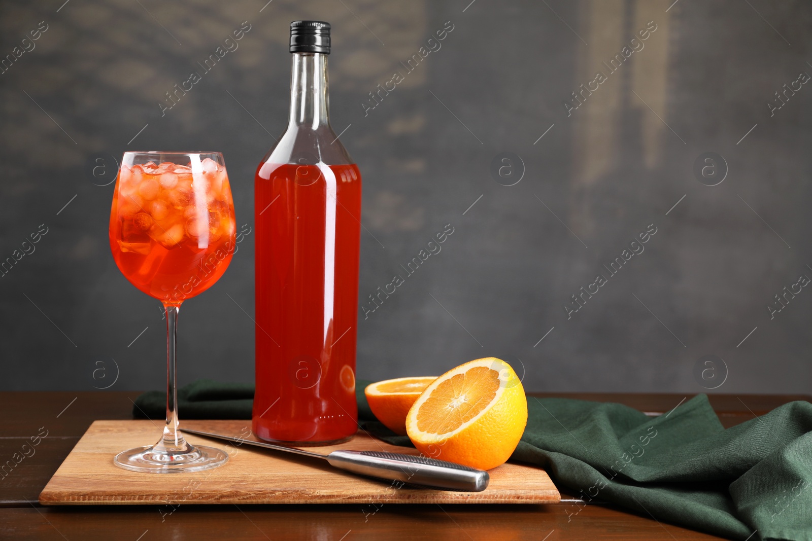 Photo of Aperol spritz cocktail and ice cubes in glass and bottle on wooden table, space for text