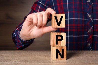 Photo of Woman making acronym VPN with cubes at wooden table, closeup