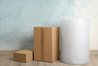 Photo of Bubble wrap roll and cardboard boxes on floor near light blue wall