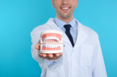 Photo of Male dentist holding jaws model on color background, closeup