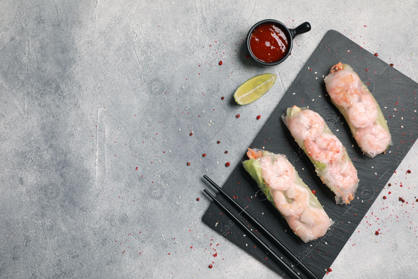 Photo of Tasty spring rolls served with spices, lime and sauce on grey textured table, flat lay. Space for text