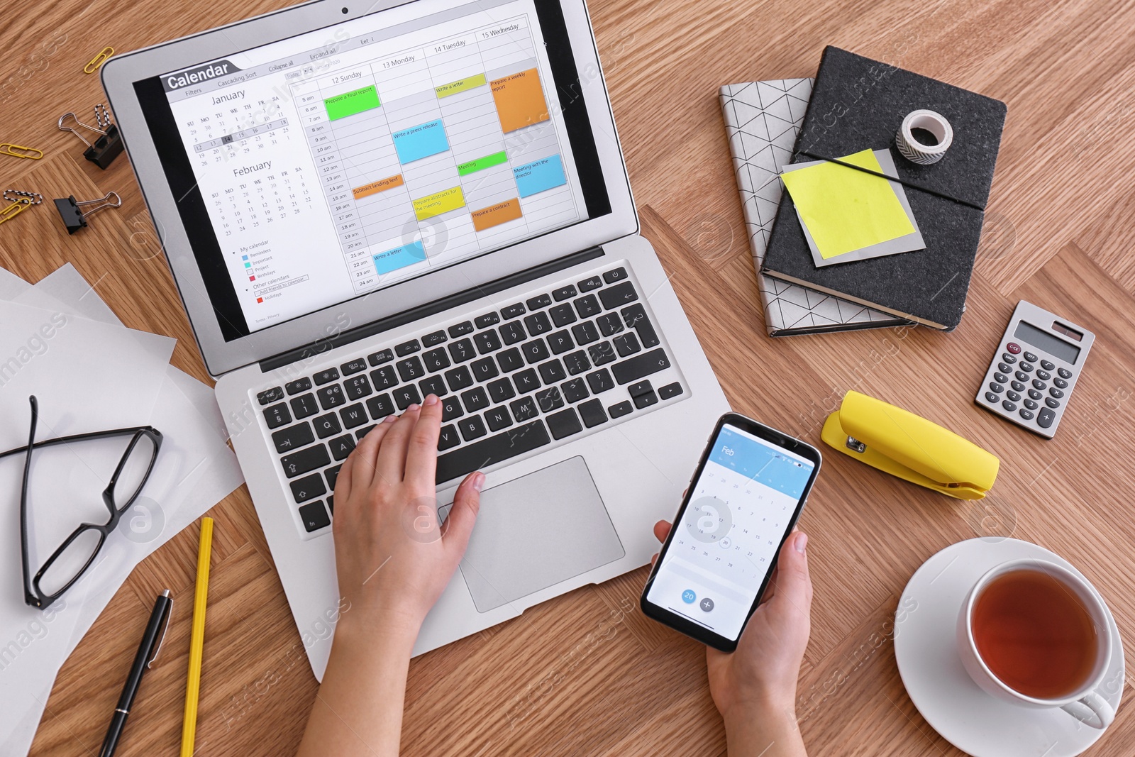 Photo of Woman using calendar on laptop and smartphone at wooden table, closeup