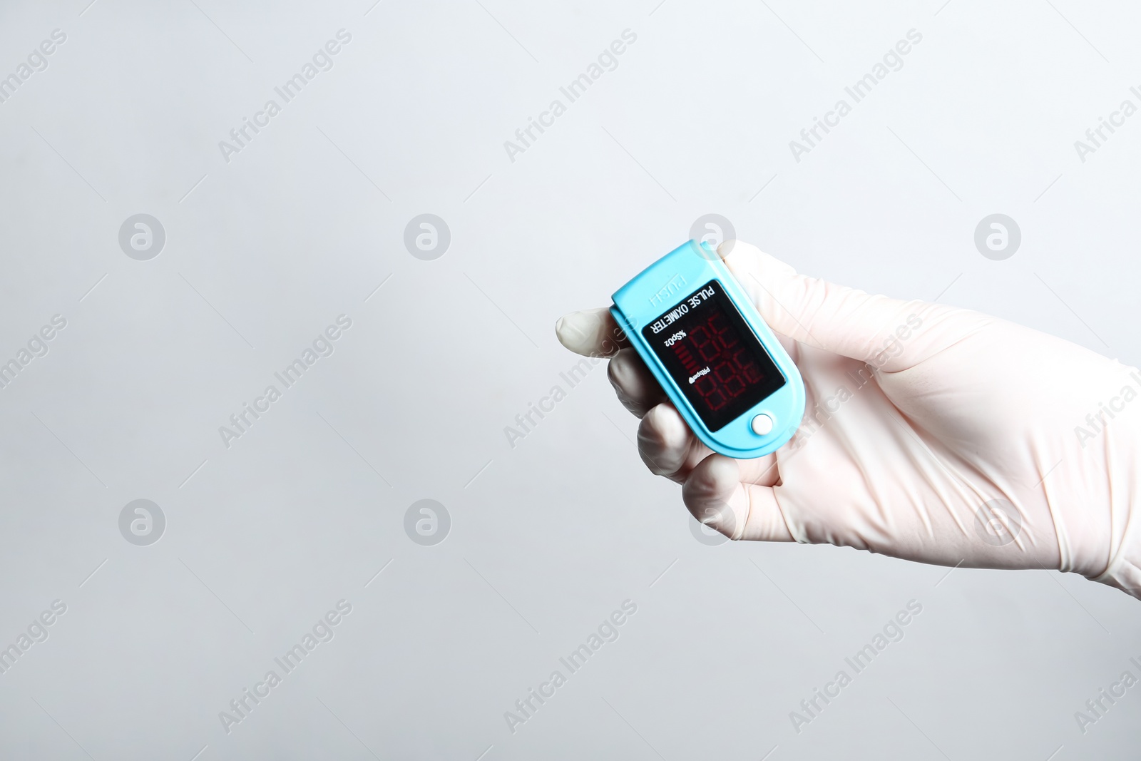 Photo of Doctor in gloves holding fingertip pulse oximeter on white background, closeup. Space for text