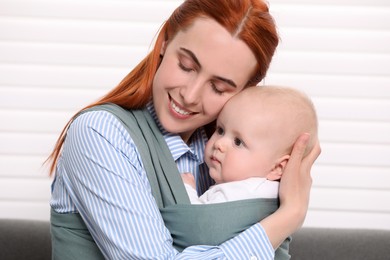 Photo of Mother holding her child in sling (baby carrier) indoors