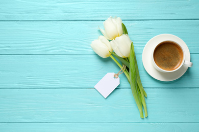 Photo of White tulips, coffee and blank tag on light blue wooden table, flat lay with space for text. Good morning