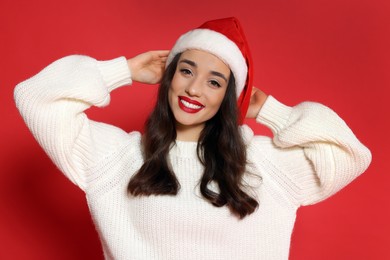 Photo of Christmas celebration. Beautiful young woman in Santa hat on red background