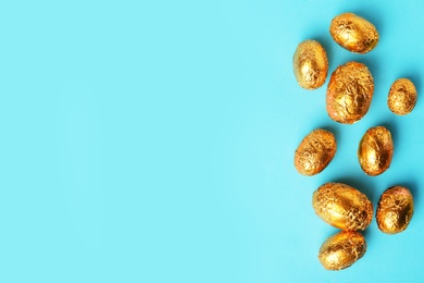 Photo of Chocolate eggs wrapped in golden foil on light blue background, flat lay. Space for text