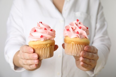 Photo of Woman holding tasty cupcakes for Valentine's Day on light background, closeup
