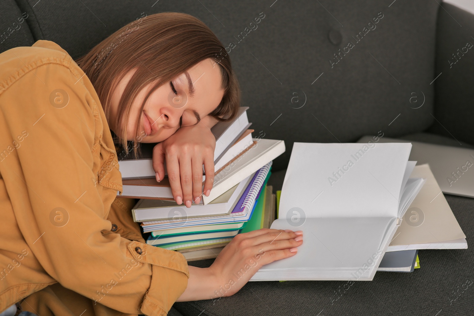 Photo of Young tired woman sleeping near books on couch