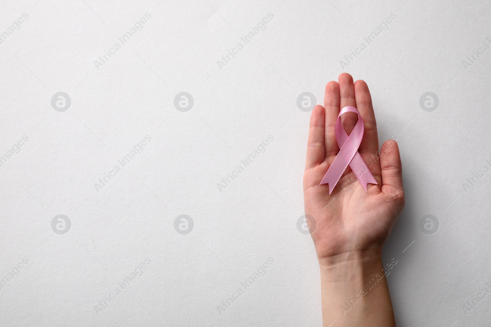 Photo of Woman holding pink ribbon on white background, top view with space for text. Breast cancer awareness concept