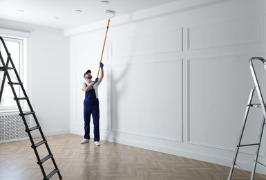 Photo of Handyman painting ceiling with white dye indoors, space for text