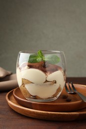 Photo of Delicious tiramisu in glass, mint leaves, coffee beans and fork on wooden table