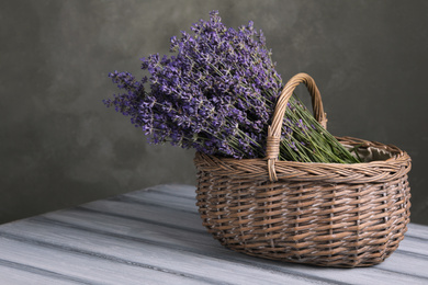 Photo of Beautiful fresh lavender flowers in wicker basket on wooden table against grey background