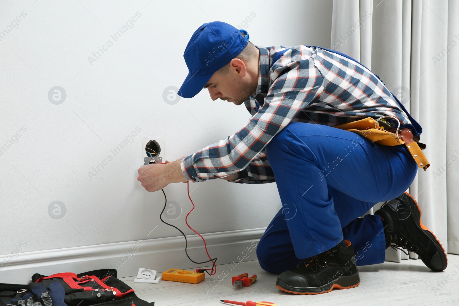 Photo of Professional electrician with tester checking voltage indoors