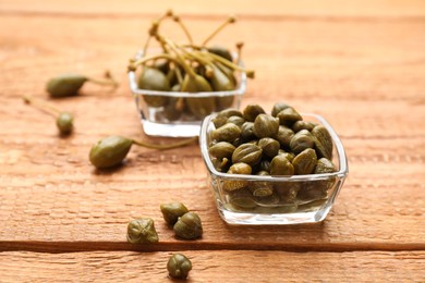 Photo of Glass bowls and delicious pickled capers on wooden table