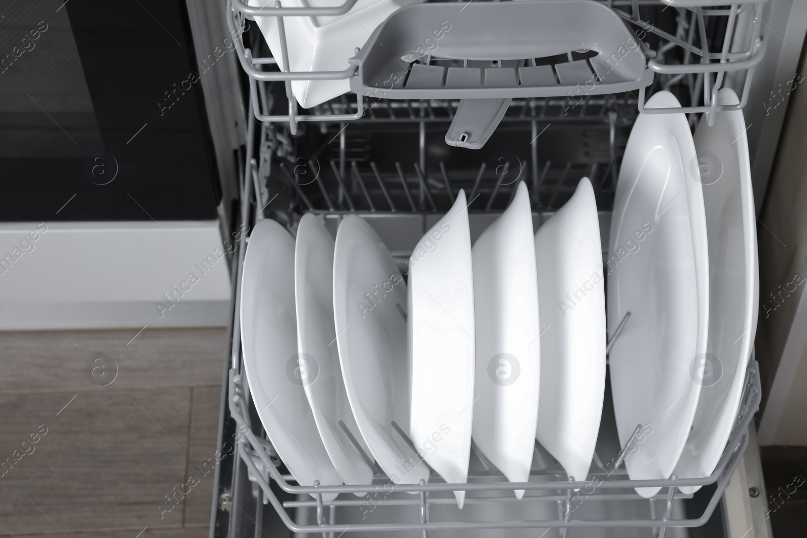 Photo of Open modern dishwasher with clean tableware, closeup