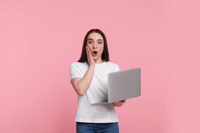 Photo of Surprised young woman with laptop on pink background