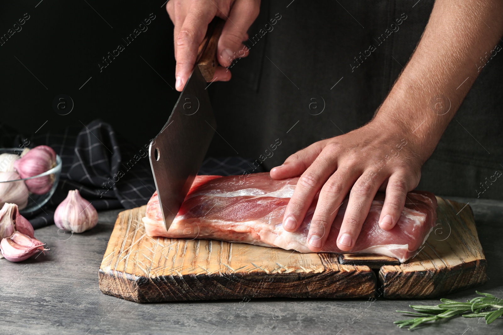 Photo of Man cutting fresh raw meat on table against dark background, closeup