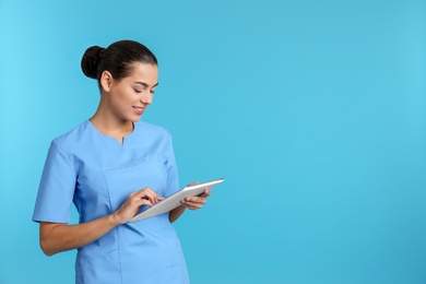 Portrait of young medical assistant with tablet on color background. Space for text