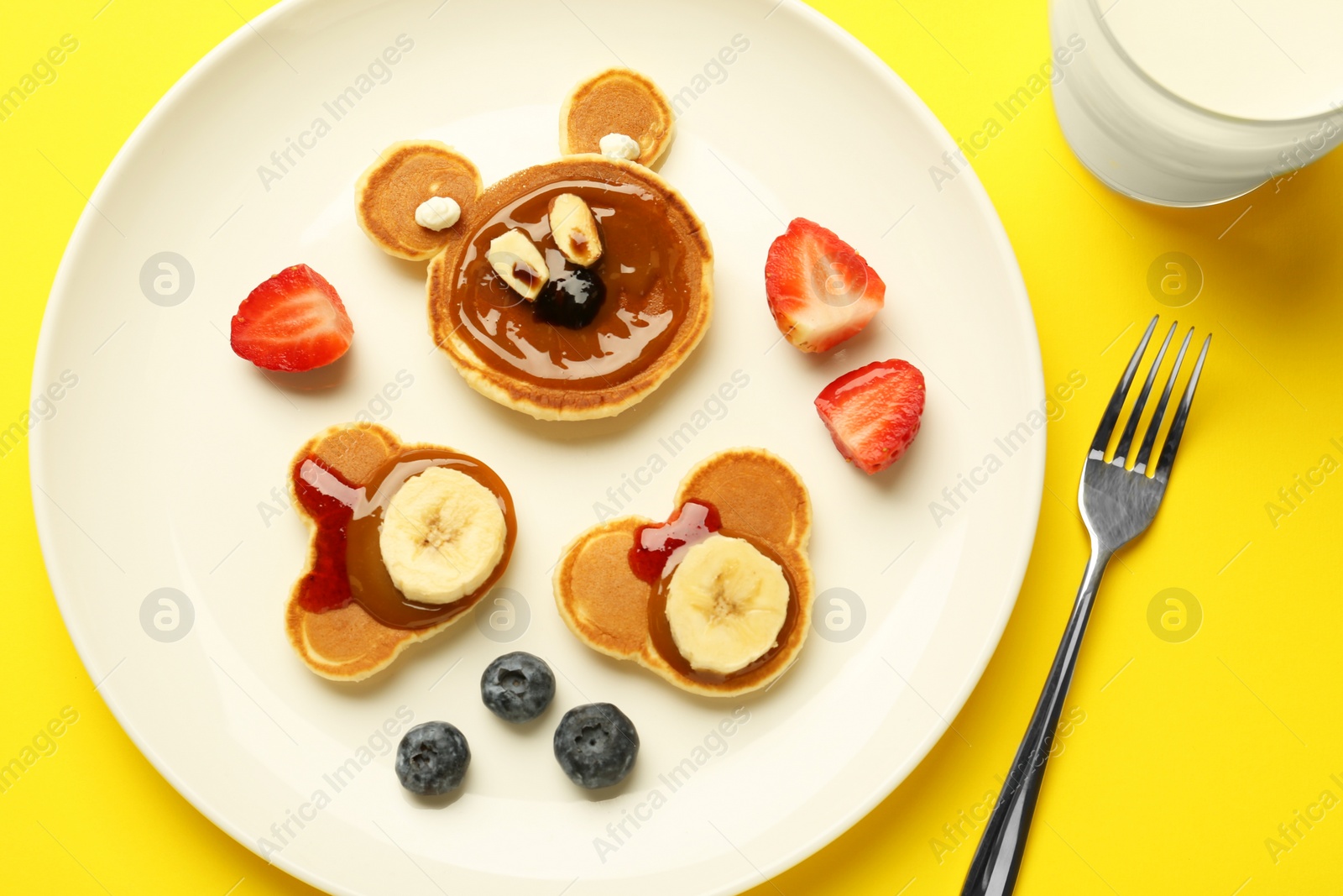 Photo of Creative serving for kids. Plate with cute bears made of pancakes, berries, banana and chocolate paste on yellow background, flat lay