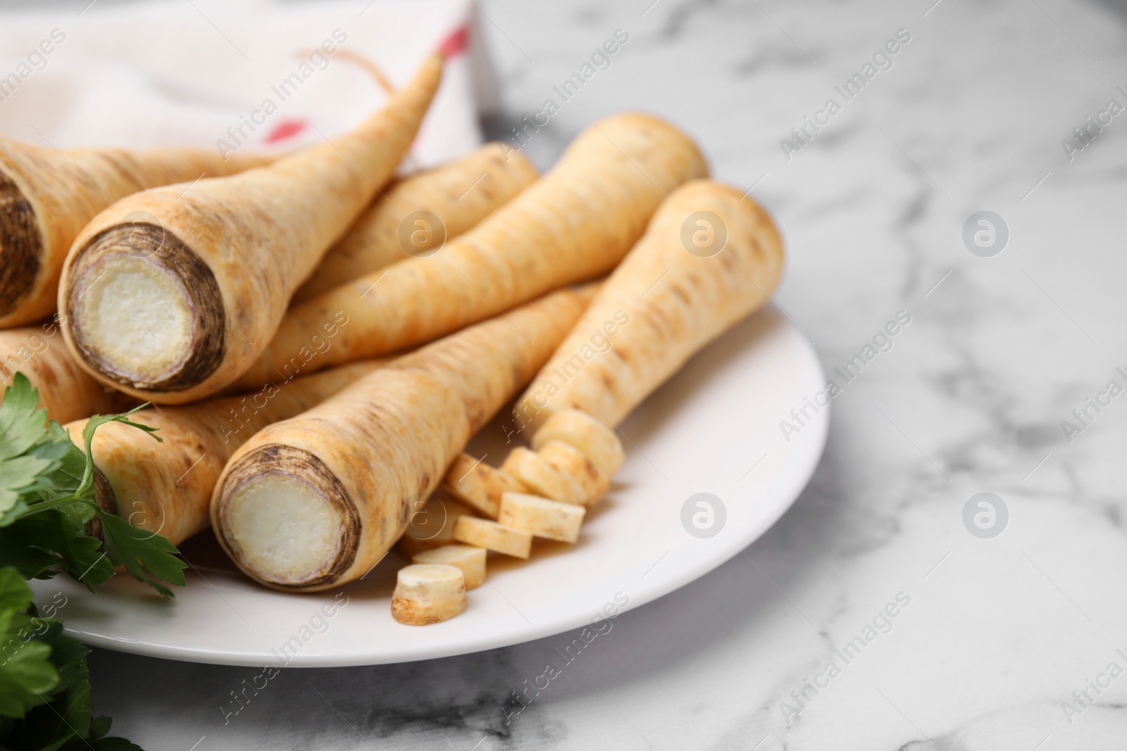 Photo of Plate with whole and cut parsley roots on white marble table, closeup. Space for text