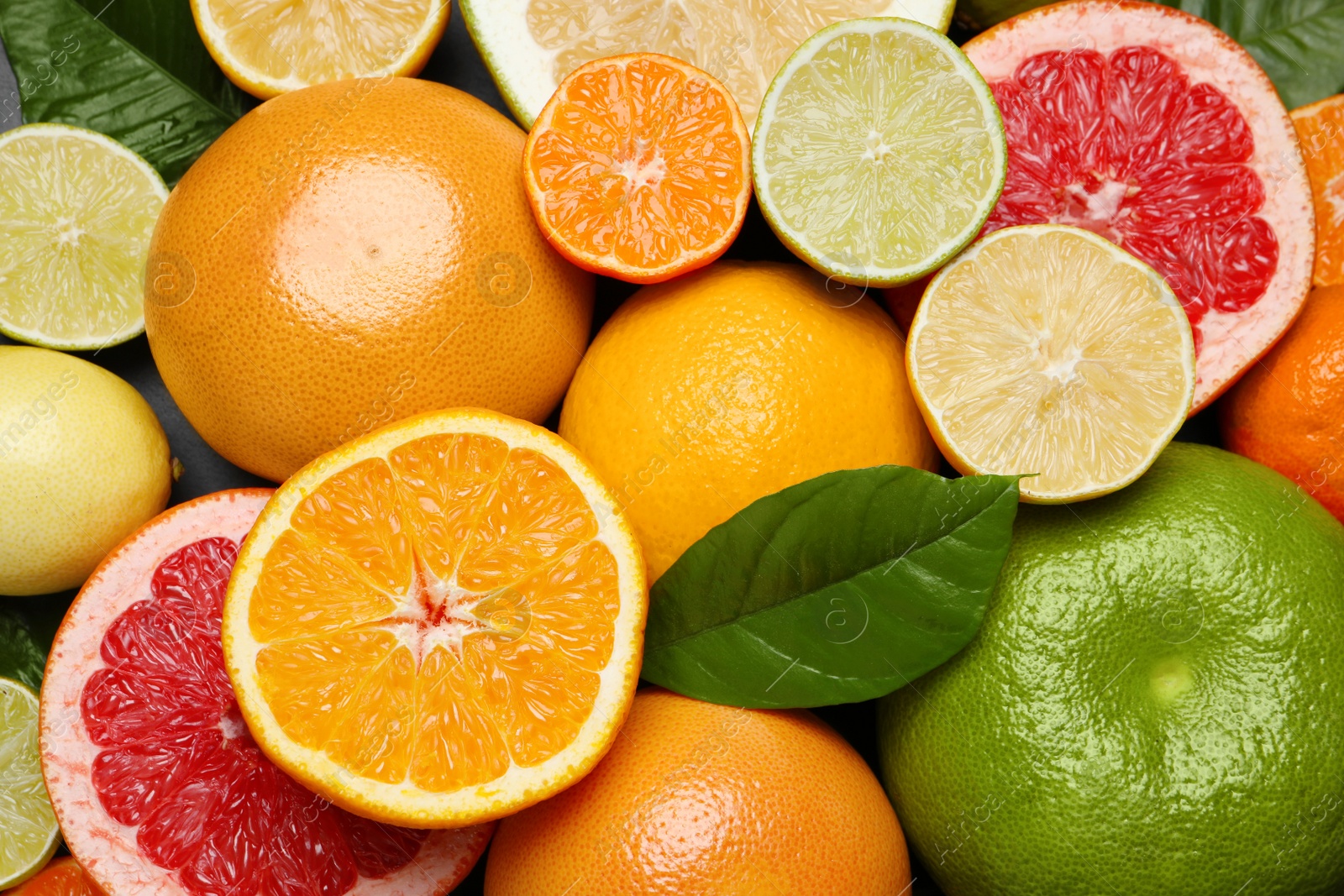 Photo of Different ripe citrus fruits with green leaves as background, top view