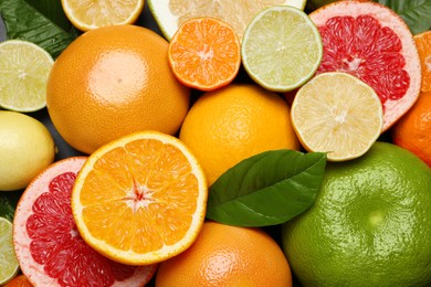 Photo of Different ripe citrus fruits with green leaves as background, top view